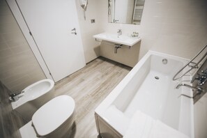 Een moderne badkamer met toilet, bidet, wastafel en bad.