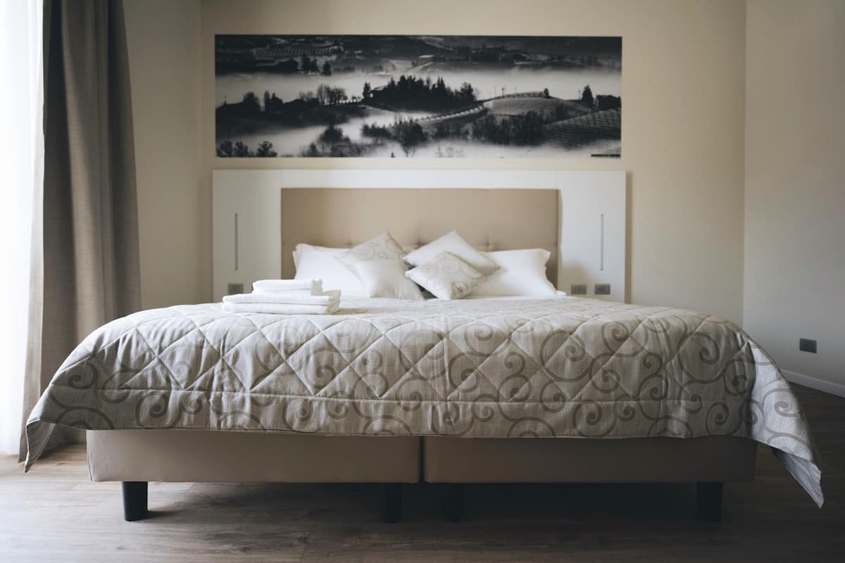 A neatly made bed with a quilted cover and pillows, a headboard, and a wall-mounted artwork above.