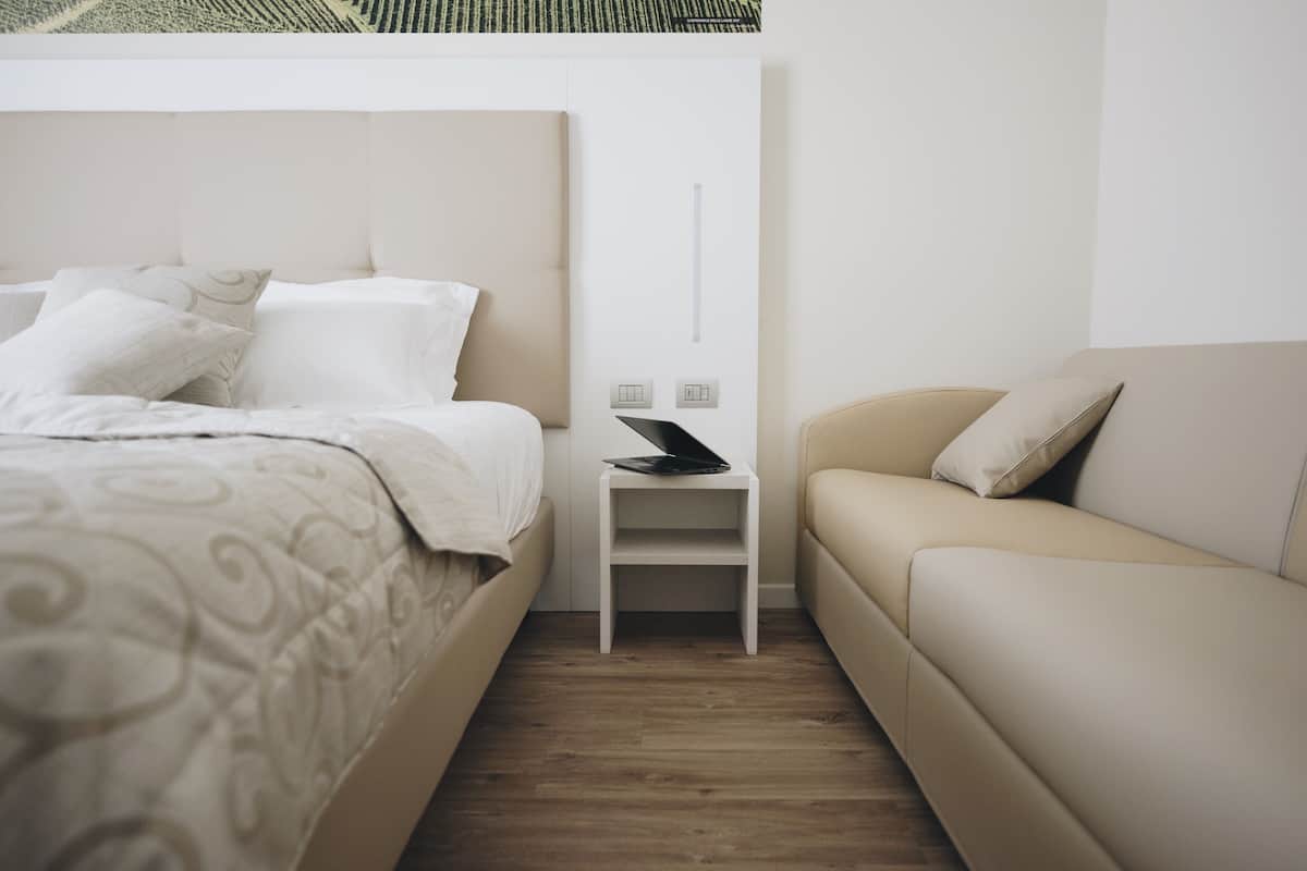 A modern bedroom with a bed, a nightstand, a laptop, and a sofa.