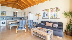 A spacious living area with a wooden ceiling, a sofa, two armchairs, a coffee table, and a kitchen in the background. - Villa Dioni-Ocean view from every room, spacious and very clean. (Magganos)