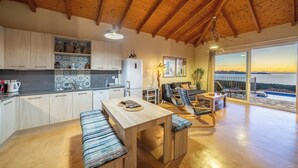 A spacious kitchen with wooden cabinets, a dining area with a bench, and a view of the sea through large windows. - Villa Dioni-Ocean view from every room, spacious and very clean. (Magganos)