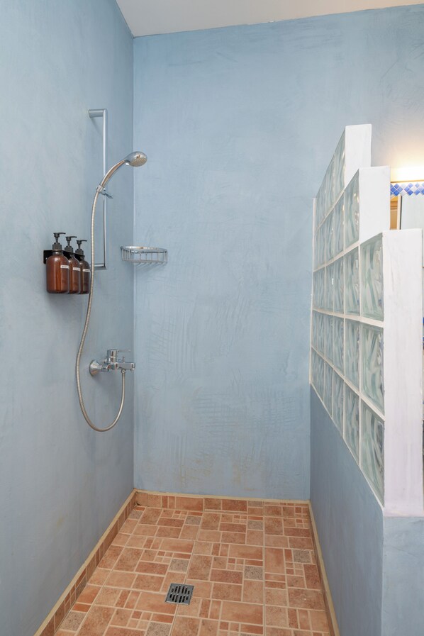 Un petit espace douche fermé, doté d’un sol carrelé, d’un pommeau de douche à main et d’un robinet fixé au mur.