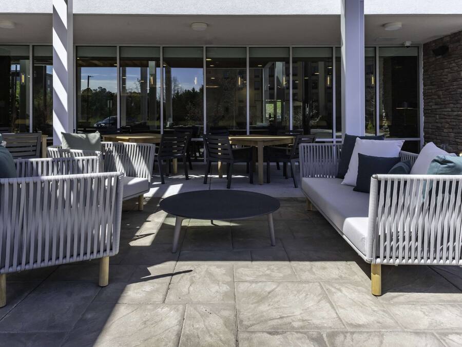 En udendørs terrasse med fletmøbler, et rundt bord og en sofa.