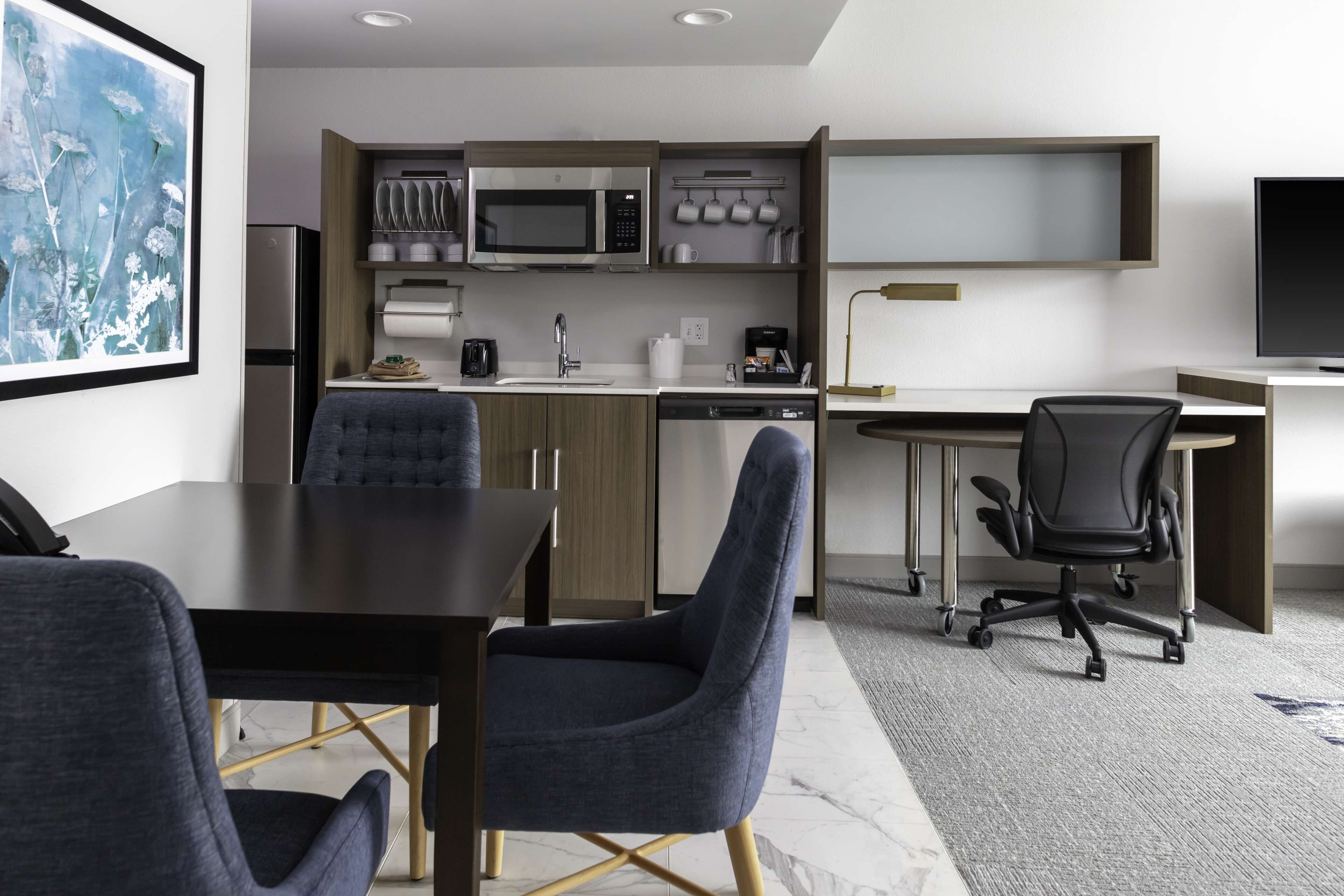 A modern kitchen with a microwave, coffee maker, and dishwasher. There is a dining area with a table and chairs, and a TV on a stand.