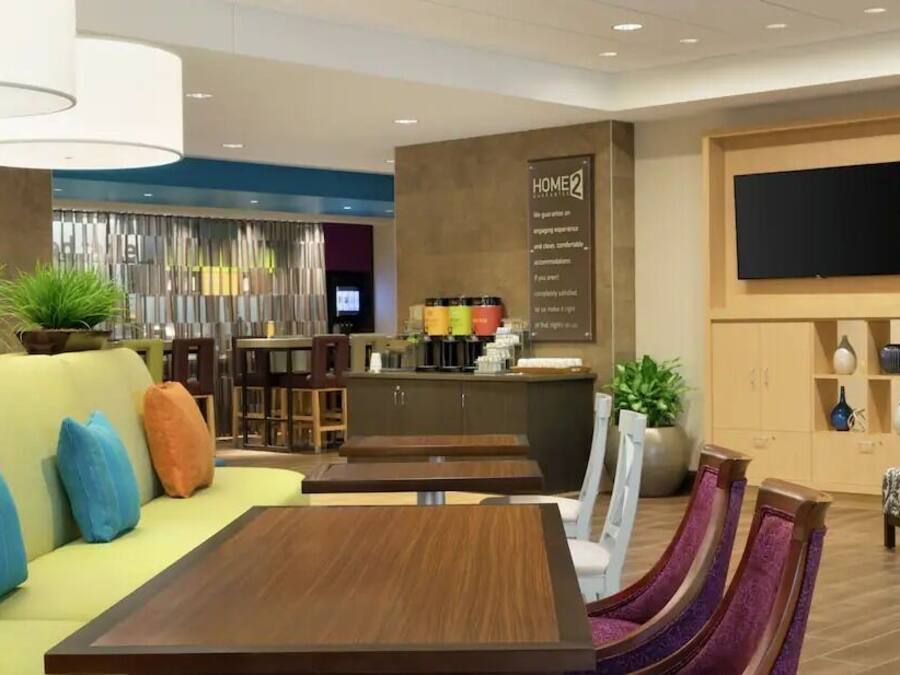 A modern hotel lobby with a sofa, dining area, and a TV mounted on the wall.