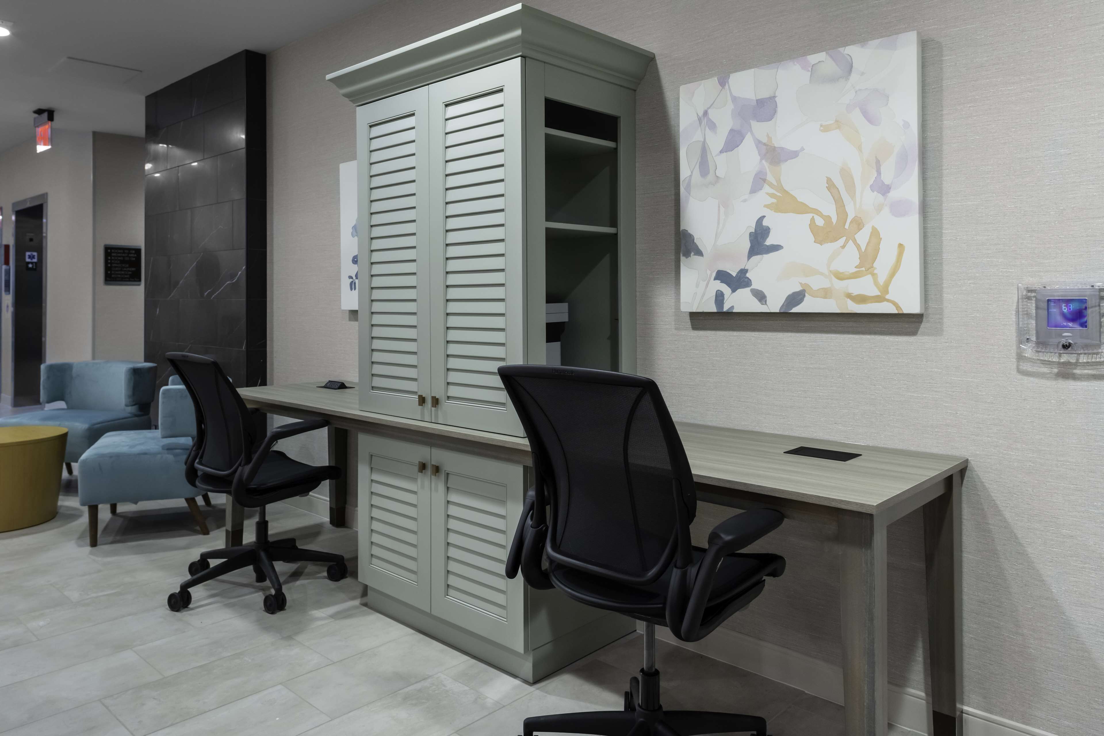 Un espace de bureau moderne avec un grand bureau, deux chaises de bureau noires, un meuble gris et un canapé bleu.