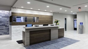 A reception area with a modern design, featuring a reception desk, a large mirror, and a digital screen. - Home2 Suites by Hilton Covington (Covington)