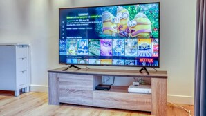 Un téléviseur à écran plat posé sur un meuble télé en bois, dont l’interface Netflix affiche différents programmes et films.