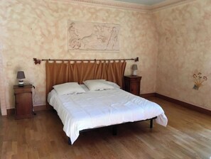 Un dormitorio con cama, suelo de madera, una mesita de noche con lámpara y una pared con estampado floral.
