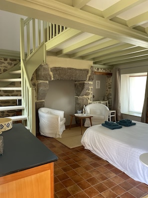 A bedroom with a bed, two chairs, a small table, a stone wall, and a staircase. - Fleur & Mer (Montfarville)