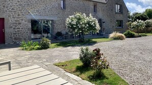 Een gebouw van steen met een grindpad, een rode deur en een tuin met witte bloemen.