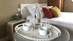 Een net opgemaakt bed met kussens en een nachtkastje met een dienblad waarop een fles, bekers en een lepel staan.