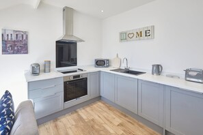 Une cuisine moderne avec des meubles gris, un four encastré, un four à micro-ondes, une bouilloire et un grille-pain.