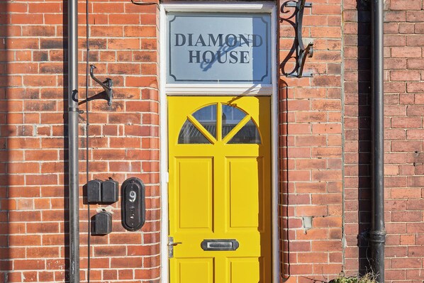 Un bâtiment en briques avec une porte jaune et une enseigne au-dessus indiquant « DIAMOND HOUSE ».