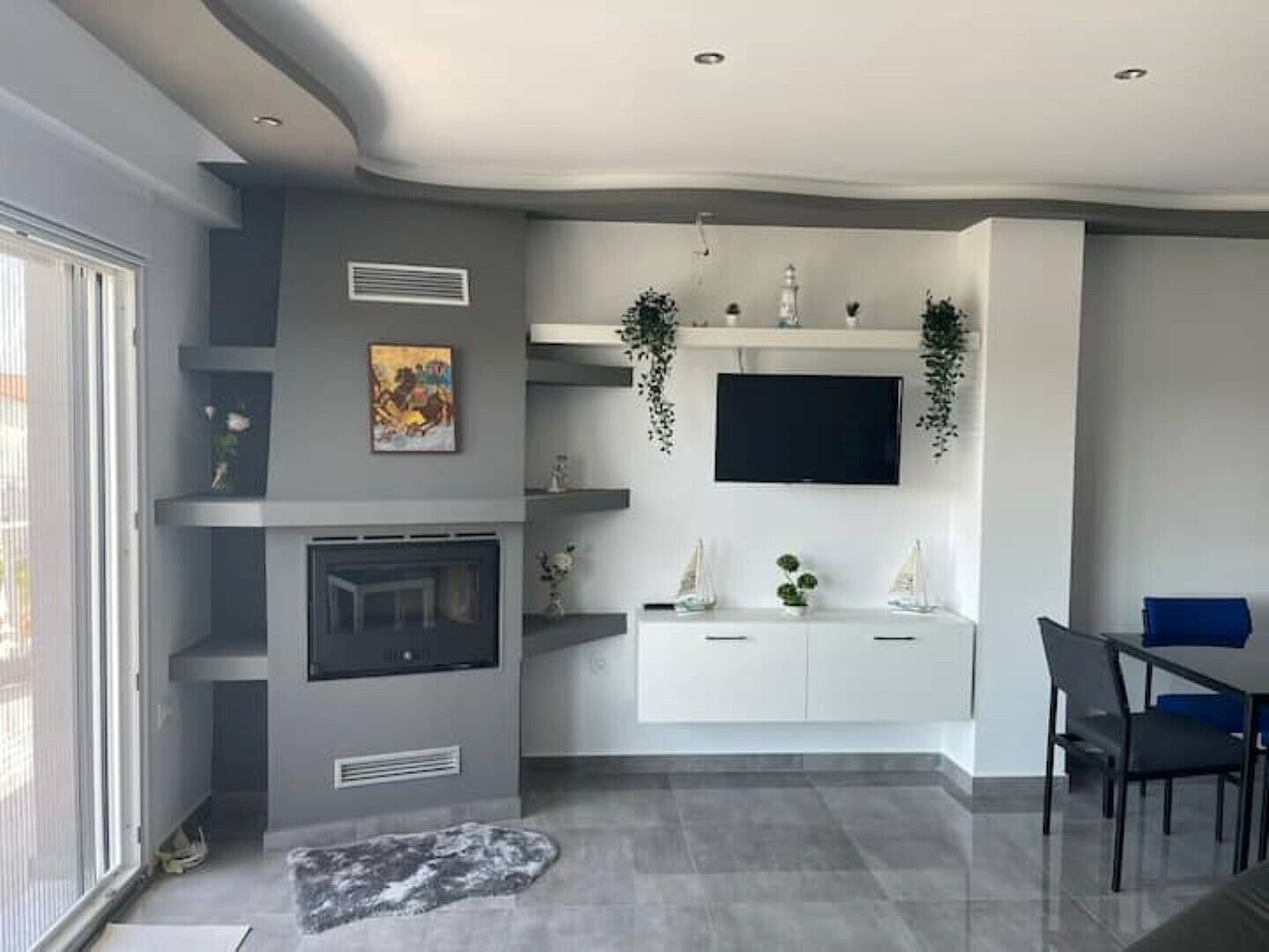 A modern living room with a fireplace, a mounted TV, and a dining area with chairs.