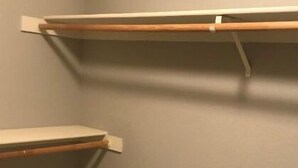 Huoneen nurkka, jossa on kolme valkoista hyllyä harmaata seinää vasten.
