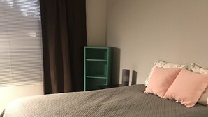 Makuuhuoneessa on sänky, vihreä hyllykkö ja ikkuna, jossa on verhot.