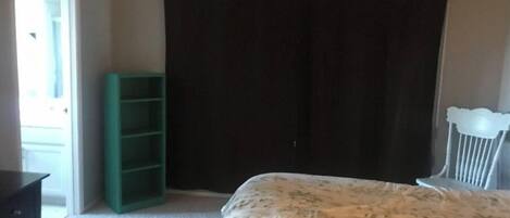 A bedroom with a bed, a green shelving unit, a white crib, and a dark curtain.