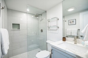 Un baño moderno con ducha envuelta en vidrio, inodoro blanco, tocador con lavabo y espejo.
