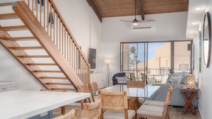 A modern interior with a wooden staircase, a dining area with wicker chairs, and a view through large windows.