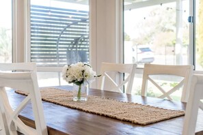 A dining table with a woven placemat, white chairs, and a vase of white flowers. - Hidden Little Gem – Luxury Township Escape in Middleton (Middleton)