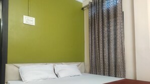 Una cama con ropa de cama blanca, una manta marrón y una pared verde con toma de corriente.