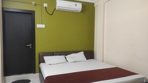 Habitación de hotel con cama, puerta, equipo de aire acondicionado y toma de corriente.