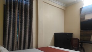 Habitación de hotel con cama, escritorio, silla, armario y televisor montado en la pared.