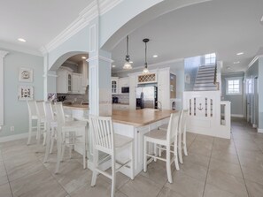 A spacious kitchen with white cabinetry, a large island with seating, and a view to the upper level.