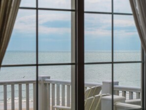 A view through a window with a railing, overlooking a calm sea and a clear sky.