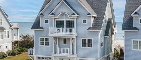 A two-story beachfront house with a balcony, a garage, and a visible address.