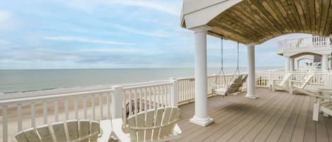 A wooden deck with white railings and chairs overlooking a beach.