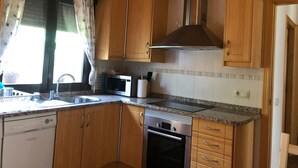 A kitchen with wooden cabinets, a stainless steel range hood, a microwave, and a dishwasher. - The flax orchard. (Candeleda)