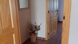 A hallway with wooden doors, a tiled floor, and a potted plant with dried plants and utensils. - The flax orchard. (Candeleda)