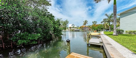 A calm river with a wooden dock, surrounded by lush greenery and palm trees.