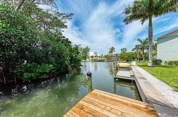 Un río tranquilo con un muelle de madera, rodeado de abundante vegetación y palmeras.