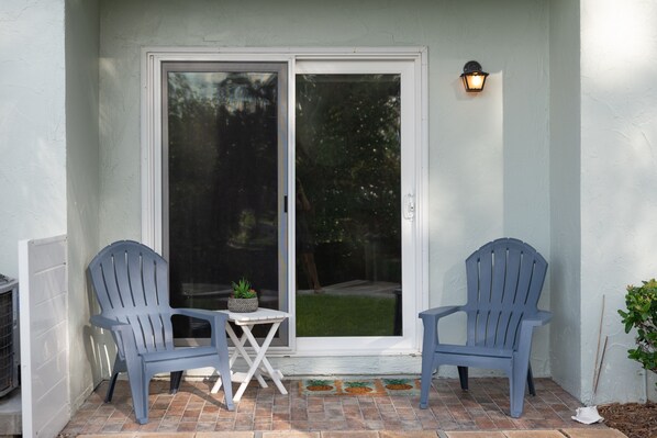 A patio with two blue Adirondack chairs, a small table, and a potted plant. - Bayou Breeze Amazing Waterfront Condo on Pine Ave with Dock and Water Views (Anna Maria)