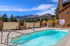 A swimming pool with a metal ladder, surrounded by a wooden fence and a mountain backdrop. - Aspen Creek #115 2 Bedroom Condo by RedAwning (Mammoth Lakes)