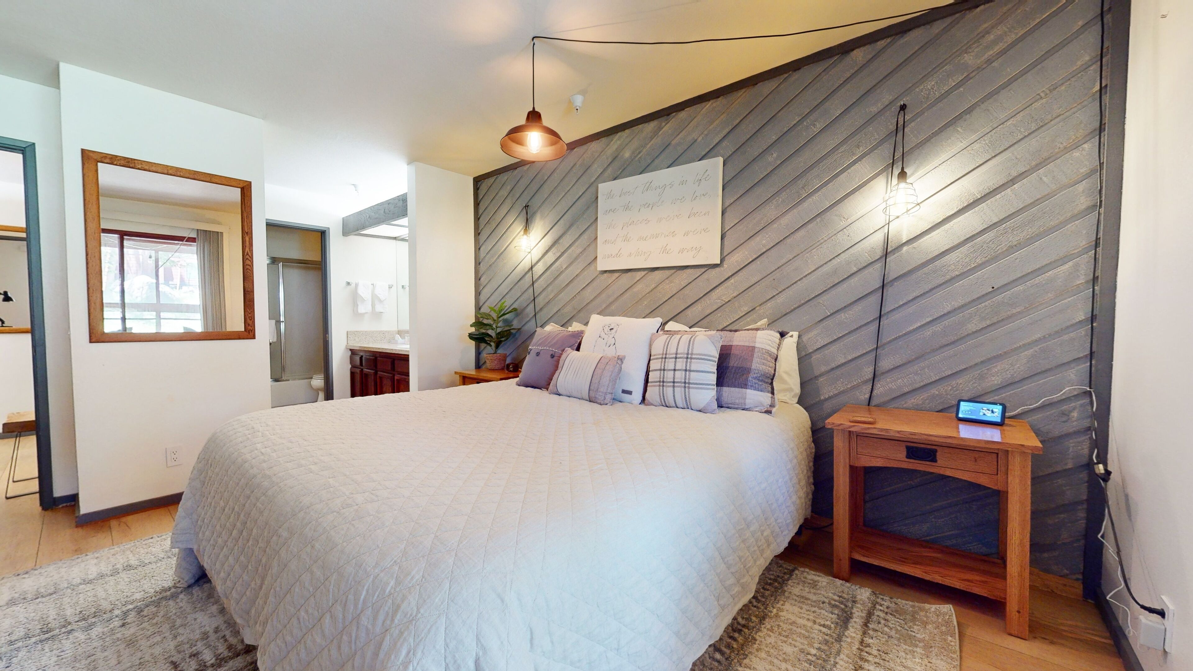 Ein Schlafzimmer mit einem großen Bett, einem hölzernen Kopfteil, einem Nachttisch, einer Wandlampe und einem Spiegel.