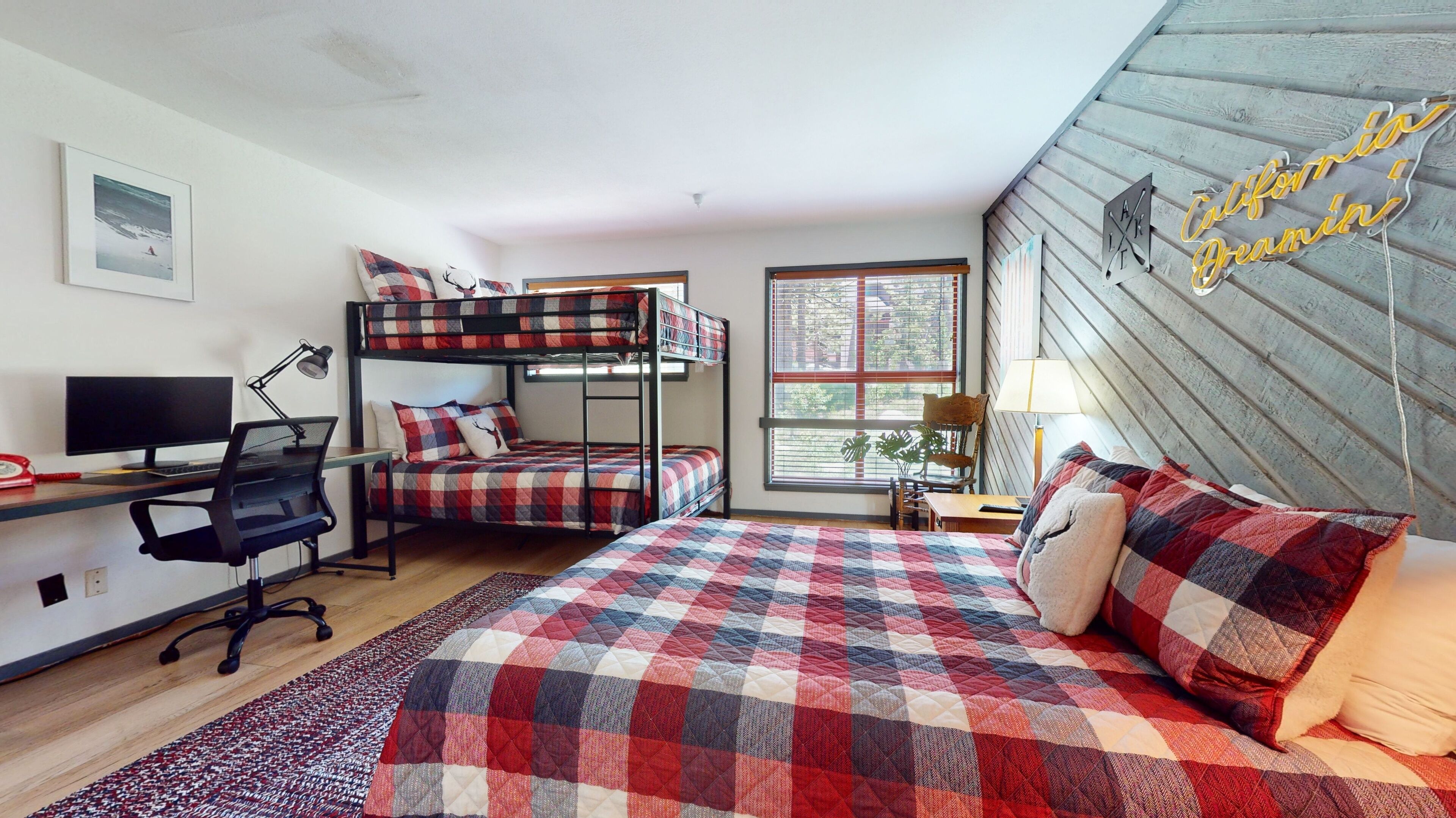 Une chambre de type dortoir, avec des lits superposés, un bureau équipé d’un ordinateur et une fenêtre avec des stores.