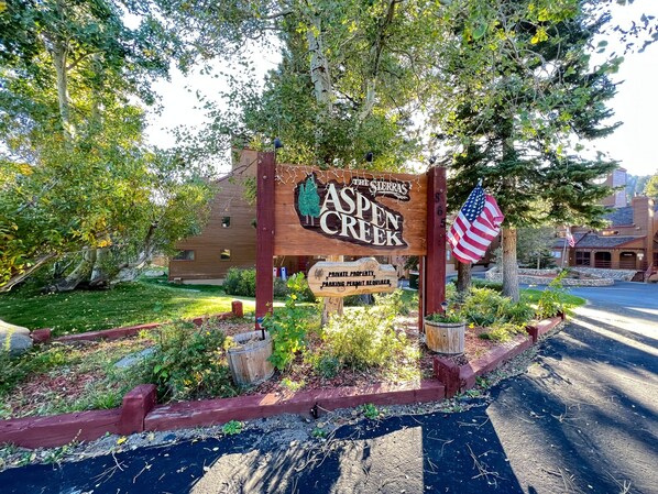 A wooden sign for Aspen Creek with a private property notice and an American flag. - Aspen Creek #115 2 Bedroom Condo by RedAwning (Mammoth Lakes)