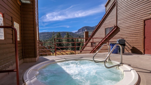 A hot tub with a view of mountains, a wooden building, and a metal staircase.