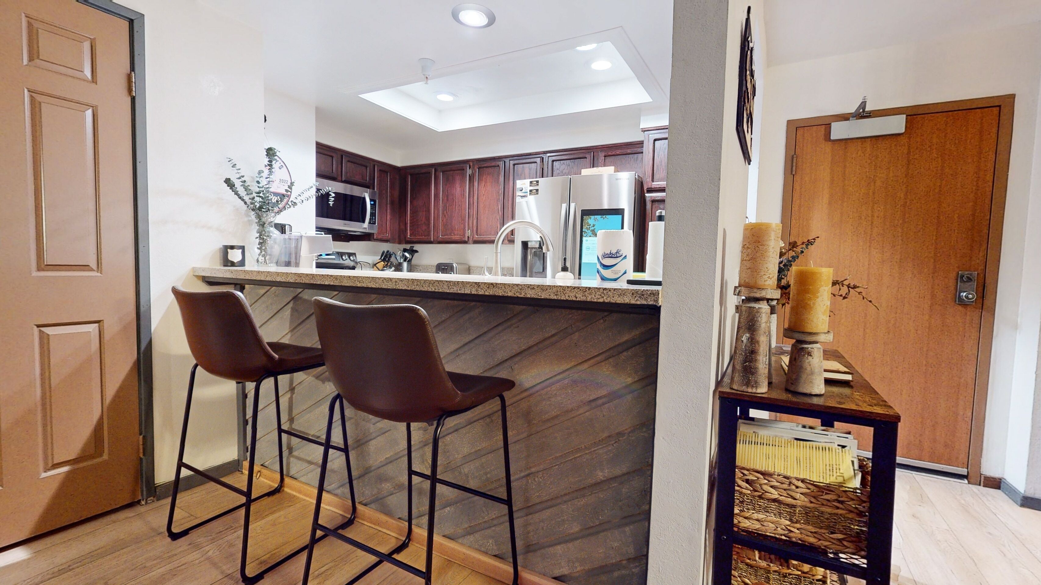 Una cocina moderna con armarios de madera oscura, electrodomésticos de acero inoxidable y una barra con dos taburetes.