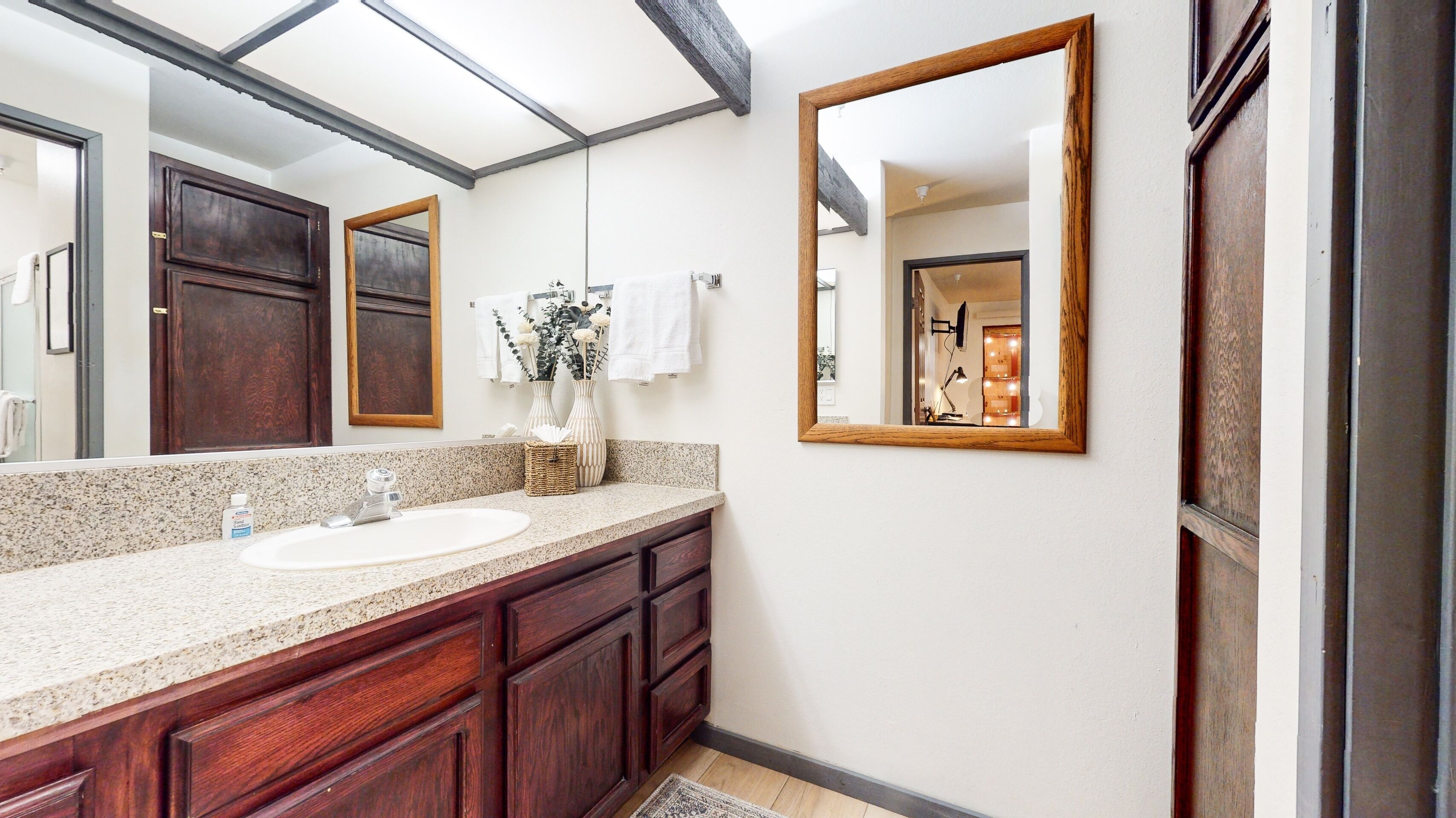 A bathroom with a large mirror, wooden cabinets, a granite countertop, and a white sink.
