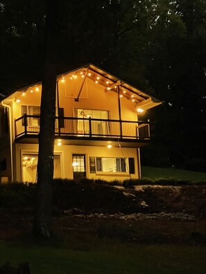 A two-story house with a balcony, illuminated by string lights.