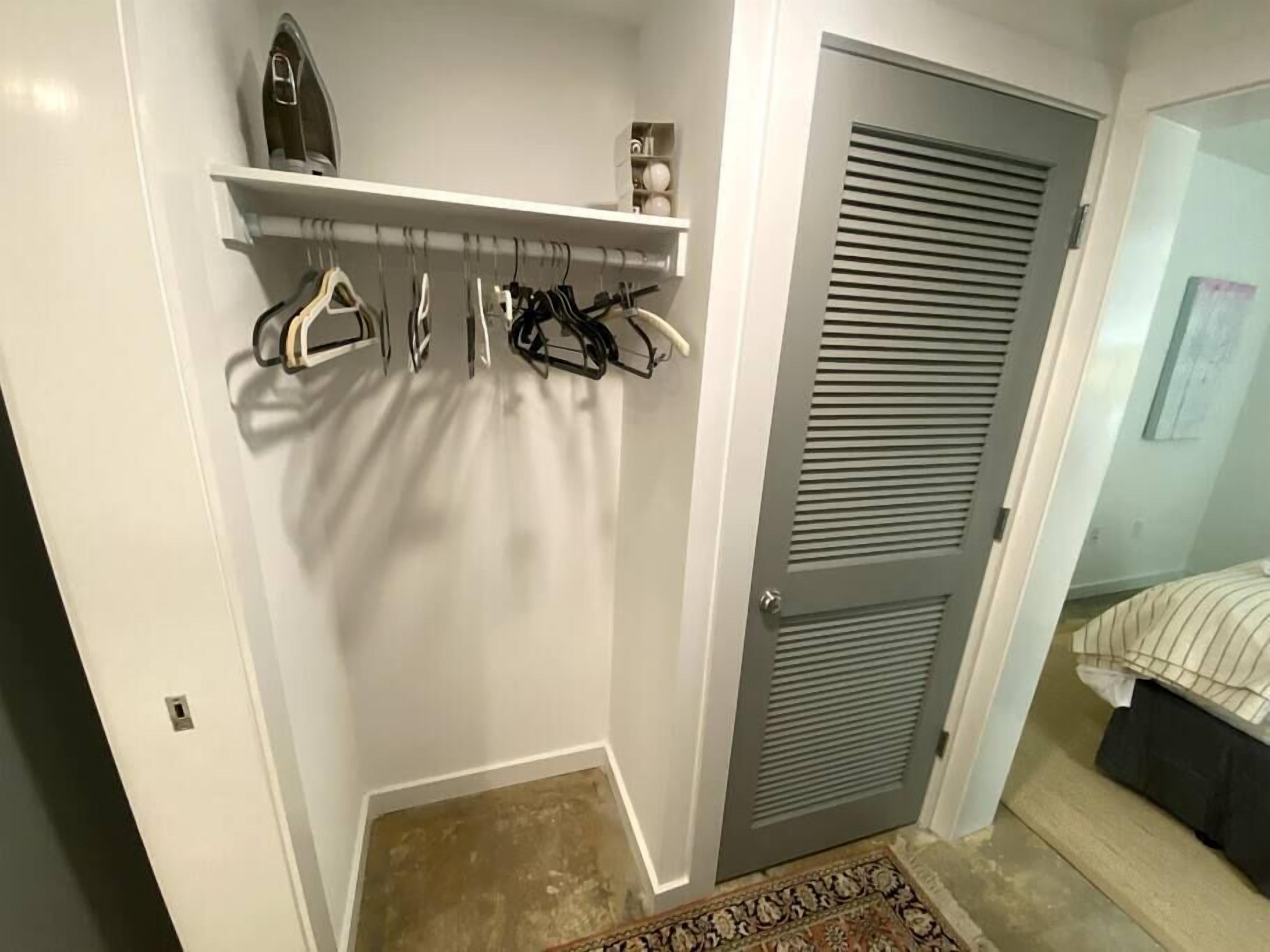 Un armario vestidor con barra para colgar, un estante con objetos decorativos y una puerta con diseño persiana.