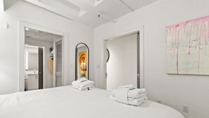 Moderni hotellihuone, jossa on suuri sänky, kaksi pyyhettä sängyllä, peili ja taulu seinällä.