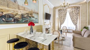 Un coin repas avec une table dressée pour quatre personnes, un lustre et une fresque représentant une scène de canal.