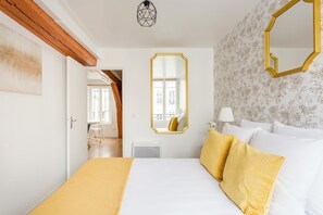 A hotel room with a bed, a large mirror, a window, and a door leading to another room.