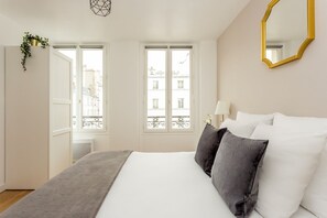 Una habitación de hotel con una cama grande, dos ventanas, un espejo y una planta.